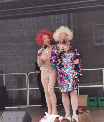 Zwei Drag-Performerinnen mit Mikrofonen stehen singend auf einer Bühne.